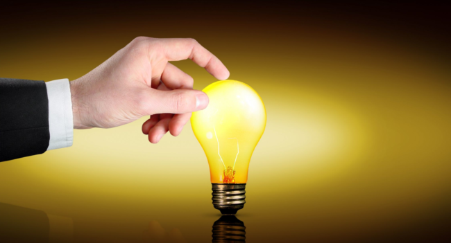 A hand reaches out to touch a glowing yellow light bulb