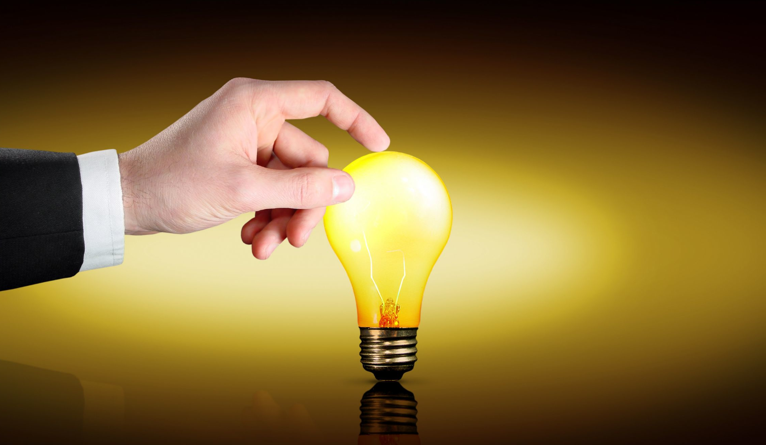 A hand reaches out to touch a glowing yellow light bulb